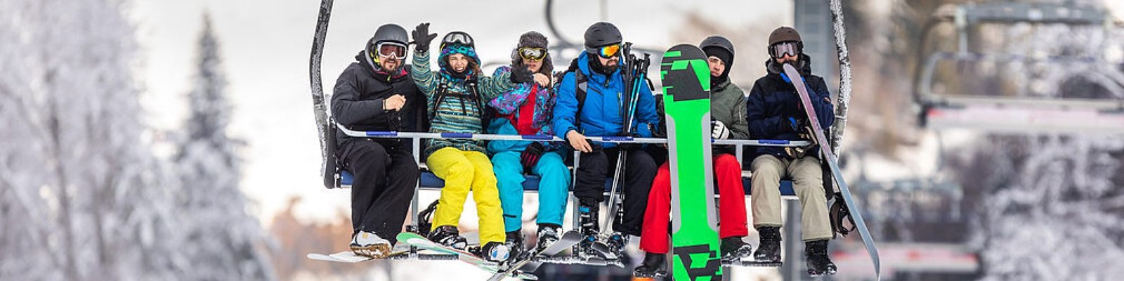 Group of happy skiers and snowboarders enjoying on a ski lift in winter day. Copy space.